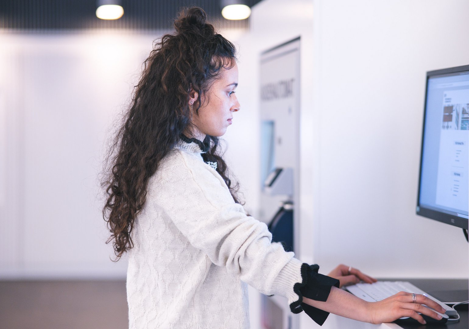Eine junge Frau steht an einem Computer und konzentriert sich auf den Bildschirm.