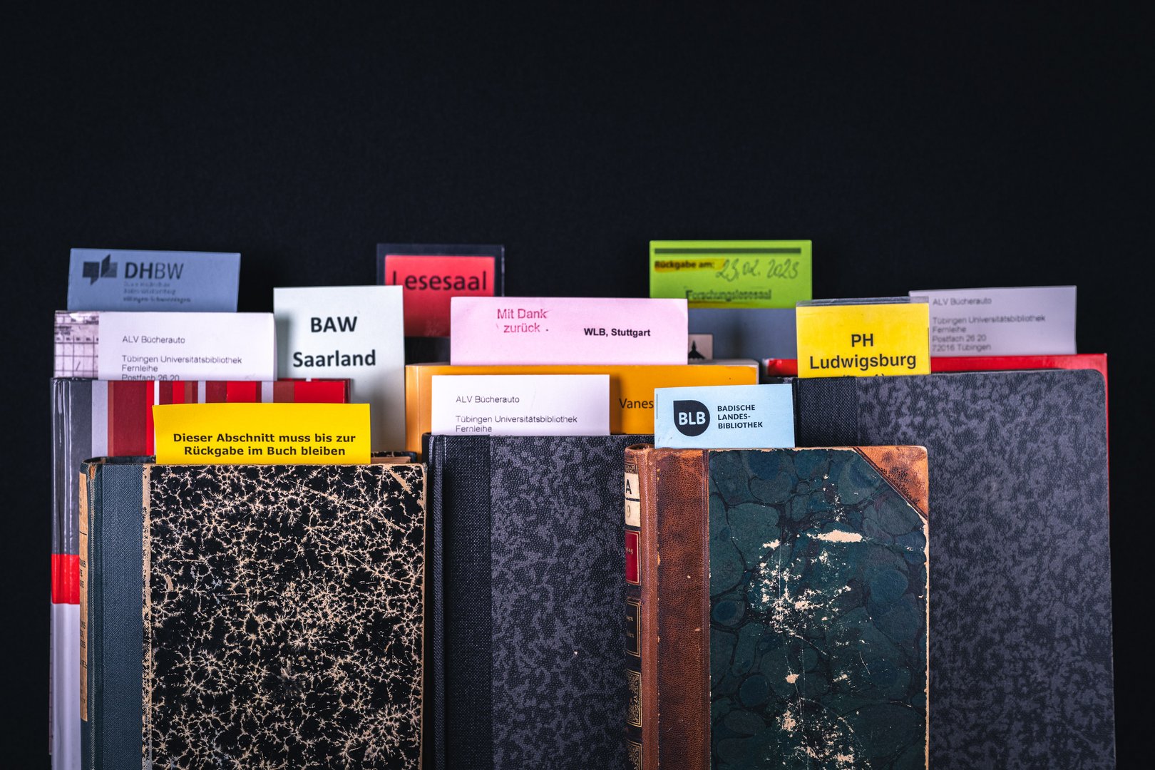 Eine Ansammlung von Büchern mit verschiedenen farbigen Etiketten, die Bibliotheksinformationen und Rückgabedaten anzeigen.
