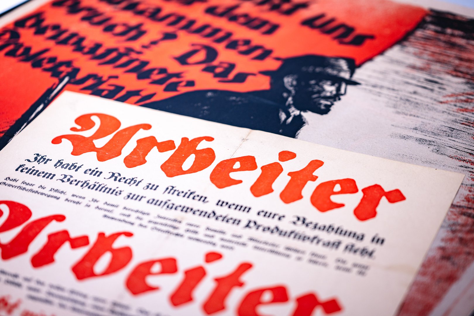 Das Bild zeigt ein Plakat, das für Arbeiterrechte wirbt, mit einer stilisierten Darstellung eines Mannes im Hintergrund.
