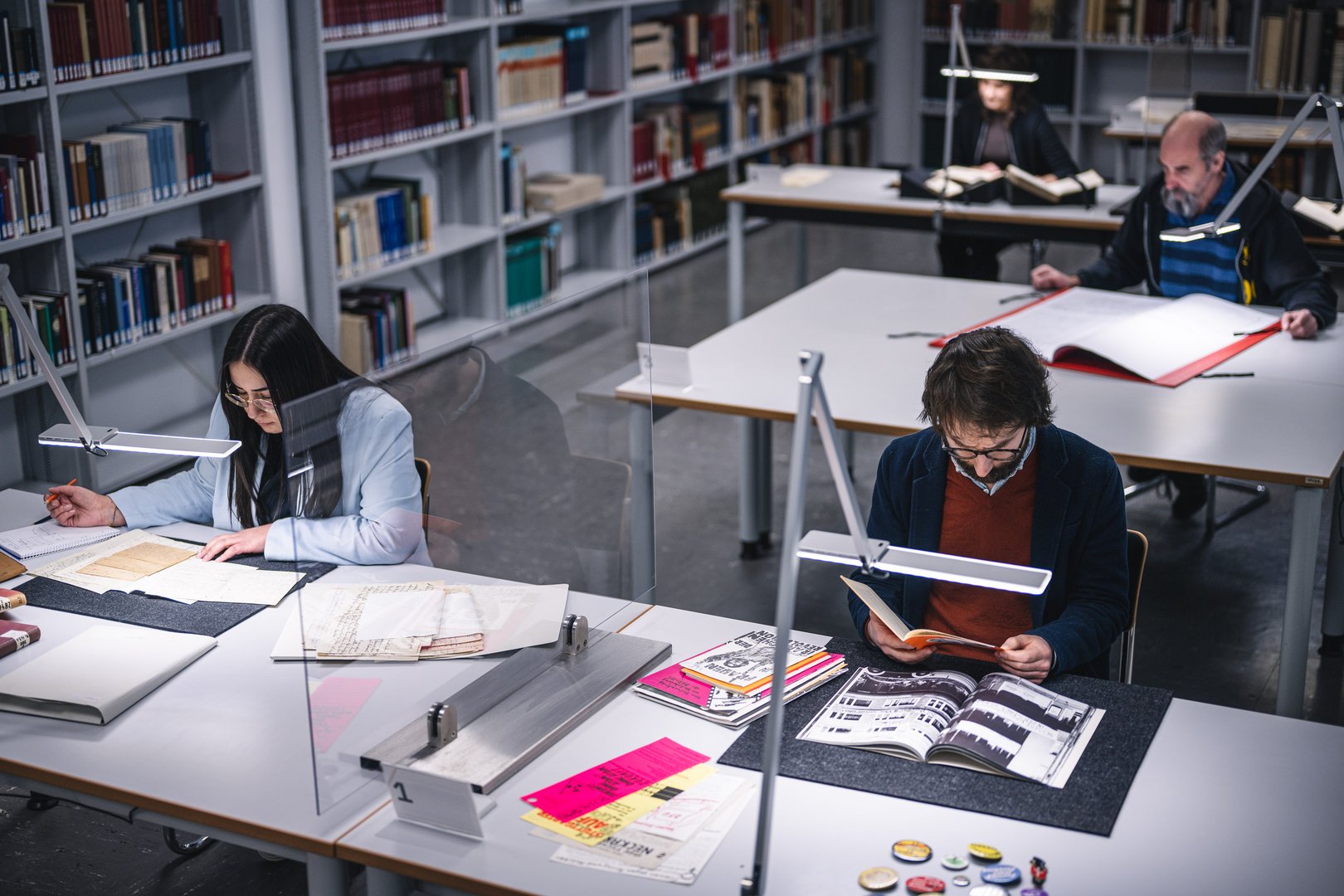 In einem modernen Lesesaal studieren mehrere Personen konzentriert an ihren Tischen, umgeben von Regalen voller Bücher.