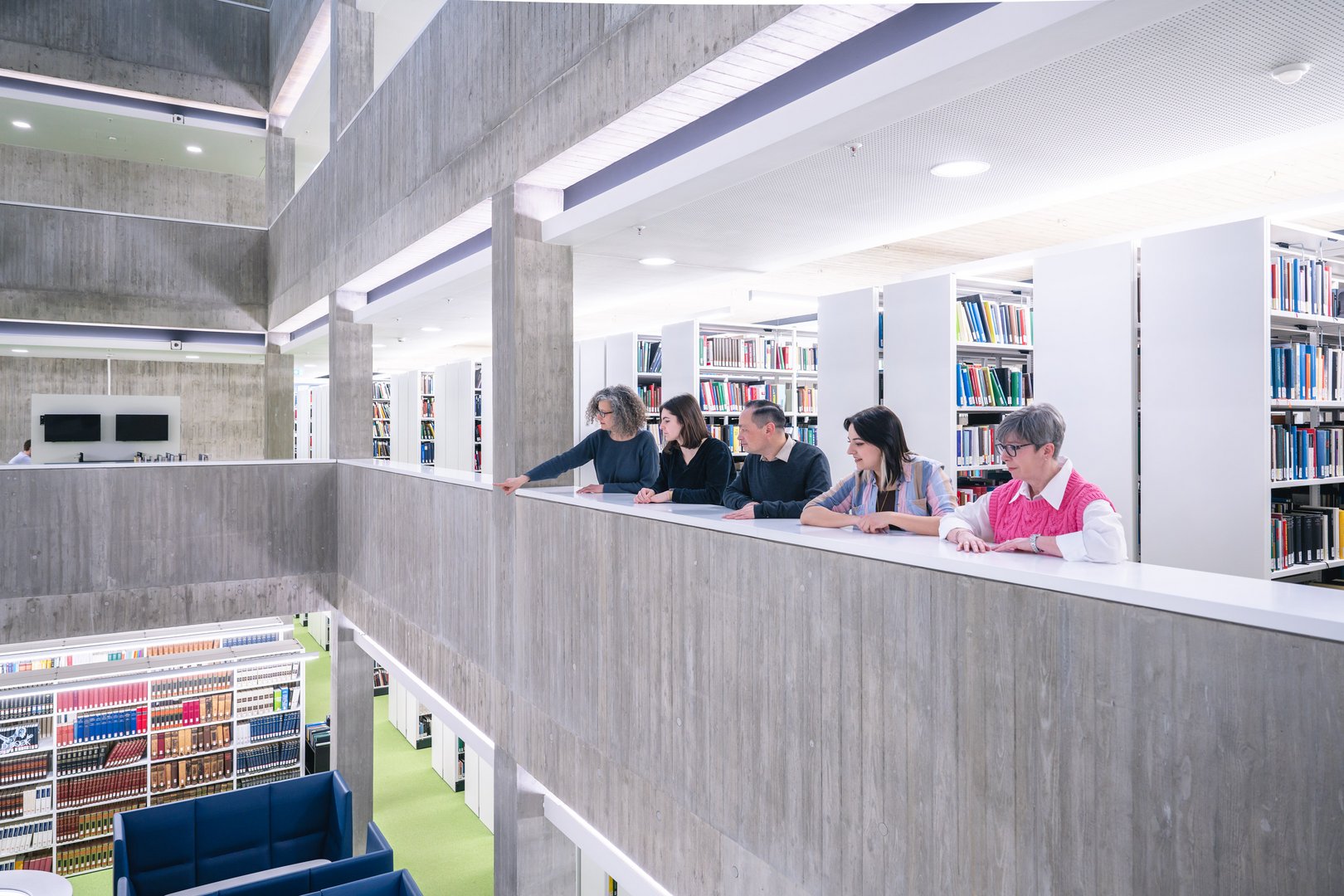 Fünf Personen stehen an einem Geländer in der WLB und schauen nach unten auf die Bücherregale.