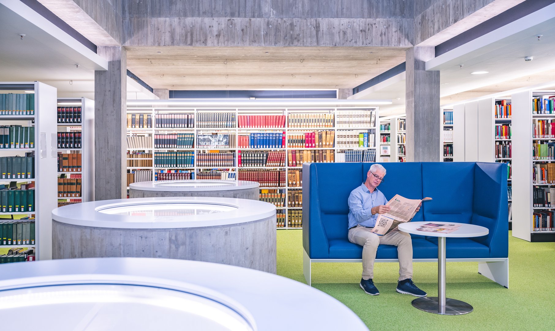In einer modernen Bibliothek sitzt ein Mann auf einem bequemen Sofa und ist vertieft in das Lesen einer Tageszeitung.
