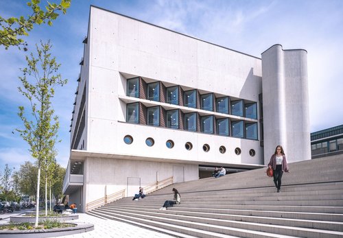 Eine Frau mit einer Tasche geht die Treppe vor der Württembergischen Landesbibliothek hinunter, während andere Menschen im Hintergrund sitzen.