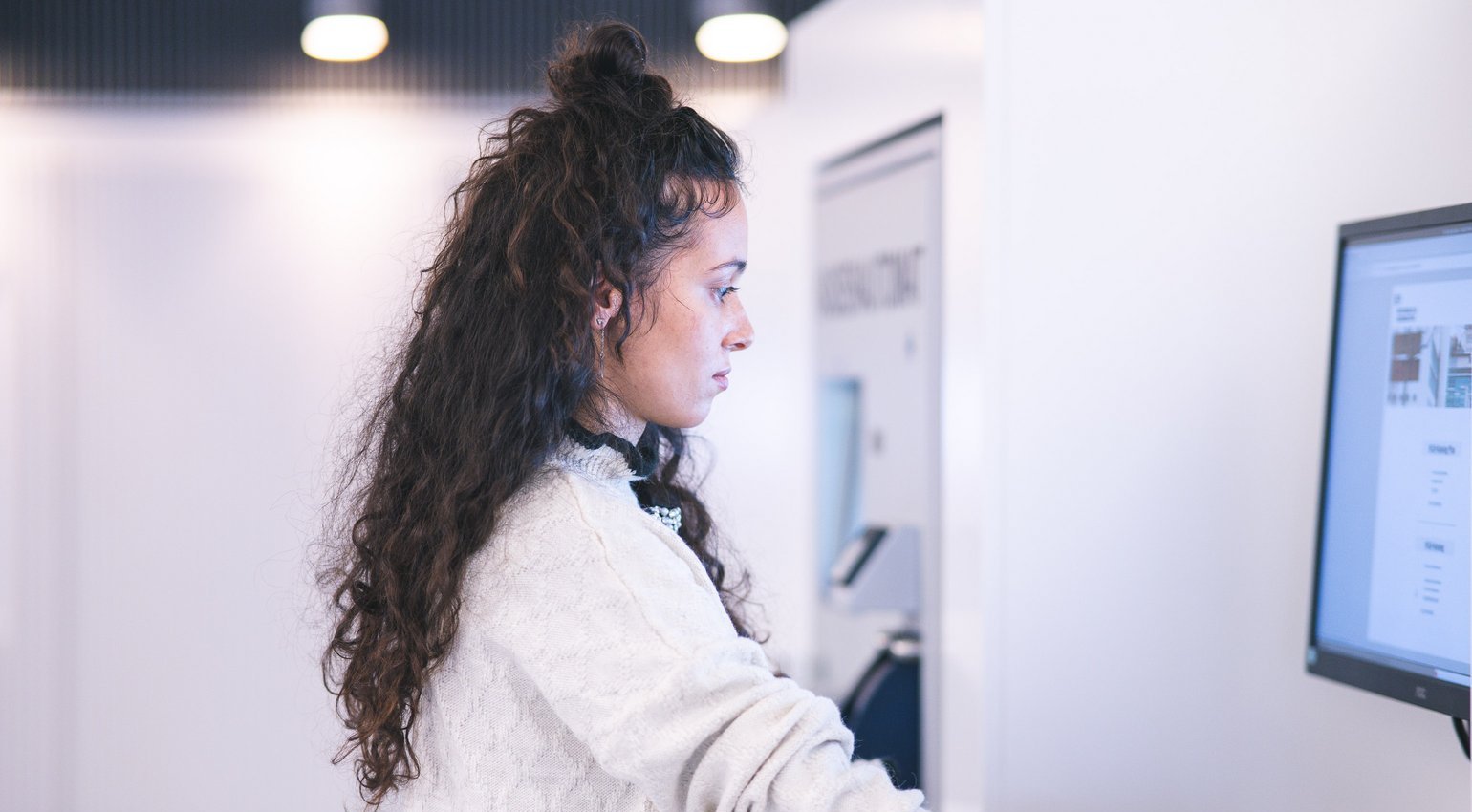 Eine junge Frau steht an einem Computer und konzentriert sich auf den Bildschirm.