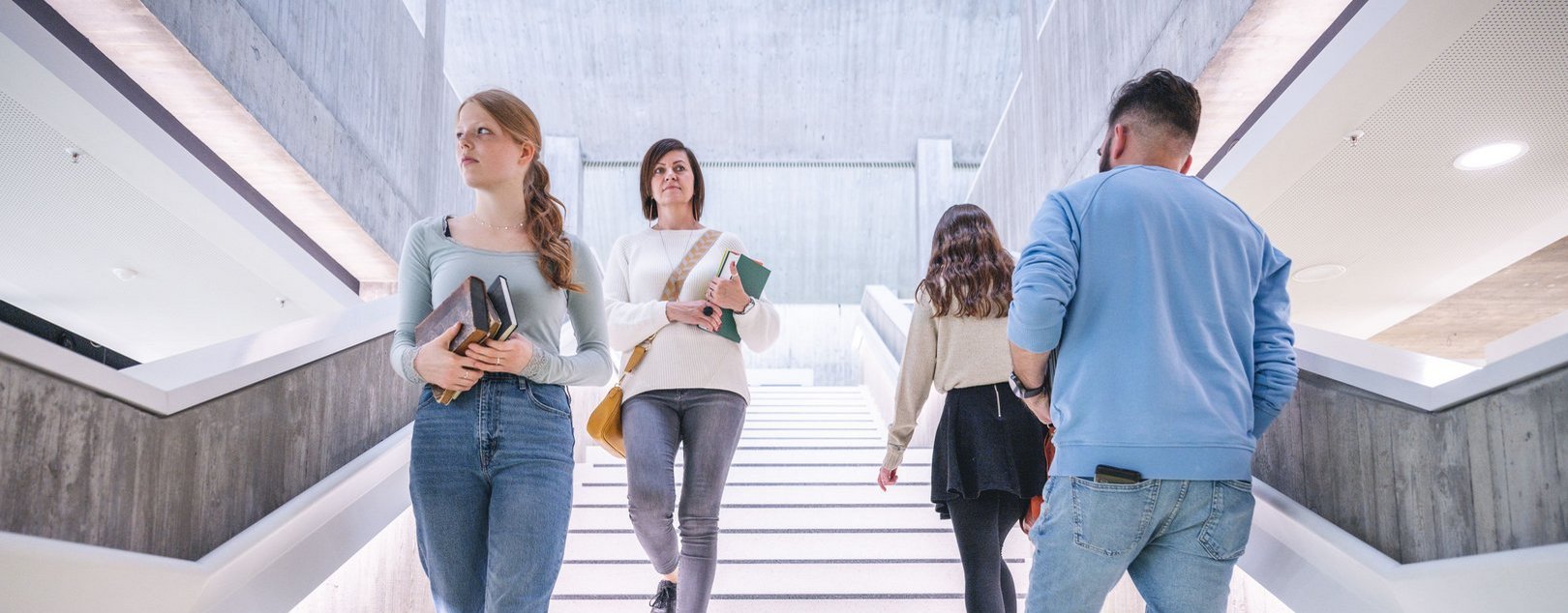 Die Szene zeigt eine Gruppe von Menschen, die in einem hellen, modernen Gebäude die Treppe nutzen.